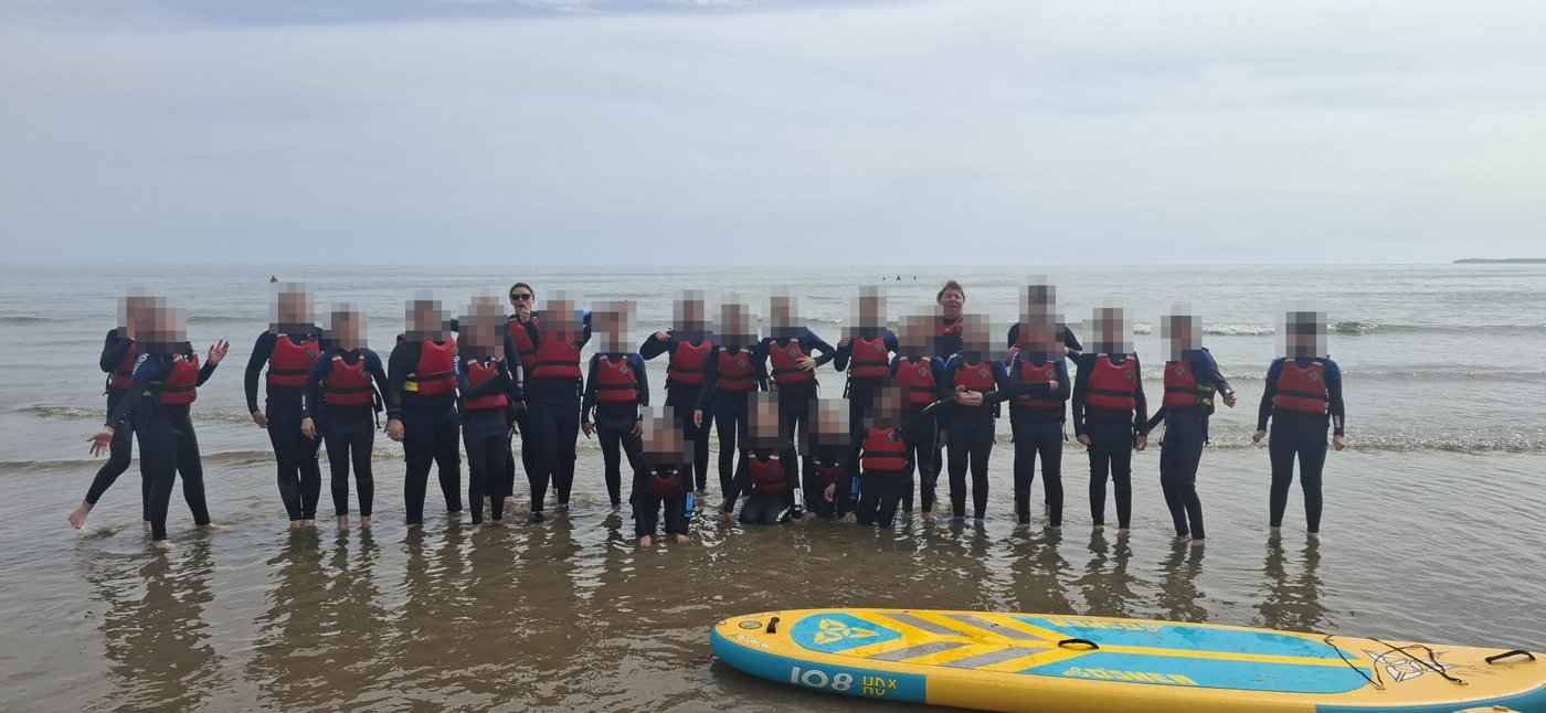 A group in wetsuits and buoyancy aids at the beach
